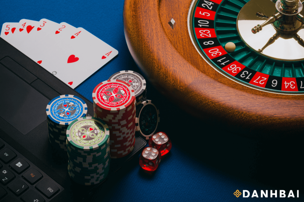 Playing cards, poker chips, two dice, and roulette wheel positioned alongside a laptop.